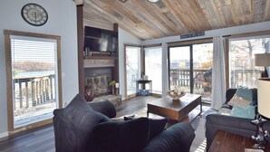 Uma sala de estar espaçosa com lareira, assentos confortáveis e amplas janelas com vista para o exterior.