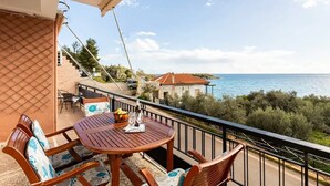 A balcony with a wooden table and chairs, overlooking a coastal view with a building and steps leading down to the sea. - Sunset Serenity - Kardamili Seaside Getaway (Kardamyli)