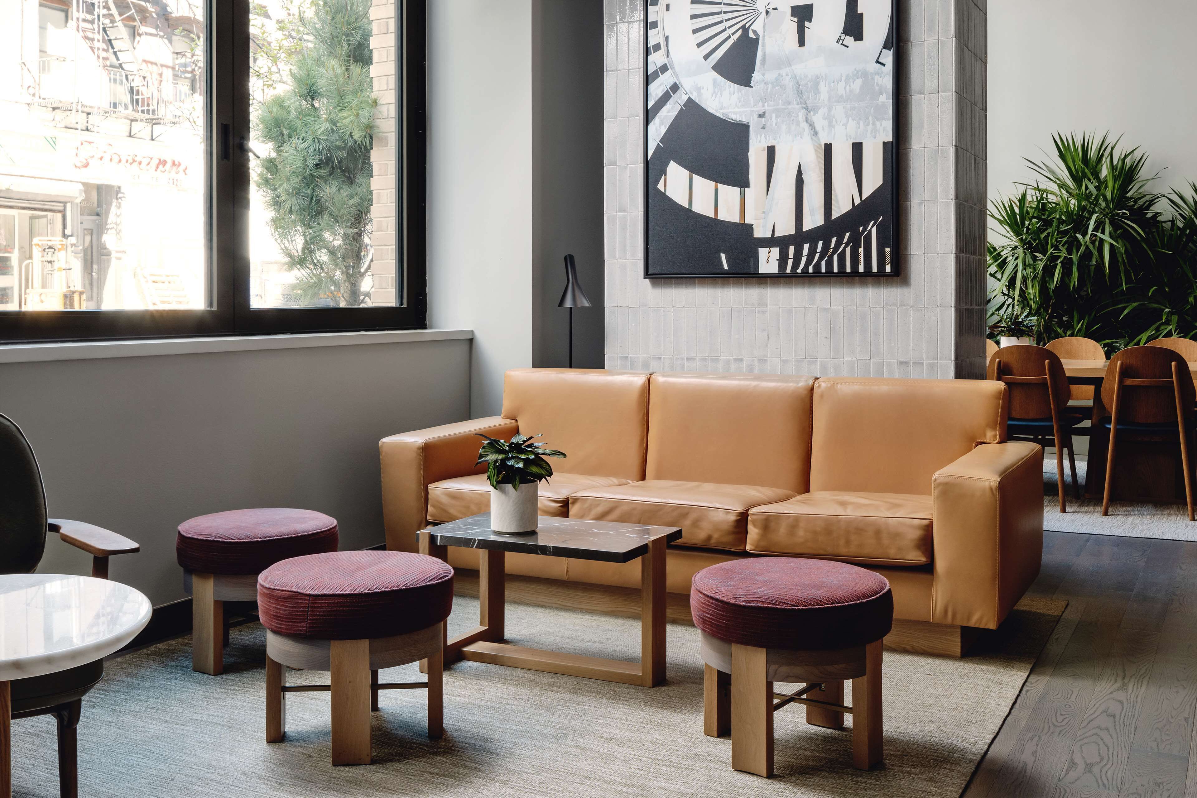 Un intérieur moderne avec un canapé en cuir, des poufs ronds, une petite table agrémentée d’une plante et un grand tableau abstrait accroché au mur.
