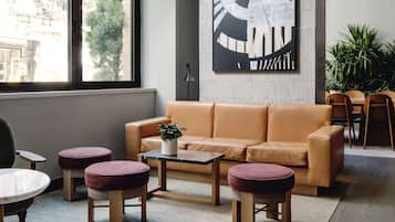 Un intérieur moderne avec un canapé en cuir, des poufs ronds, une petite table agrémentée d’une plante et un grand tableau abstrait accroché au mur.