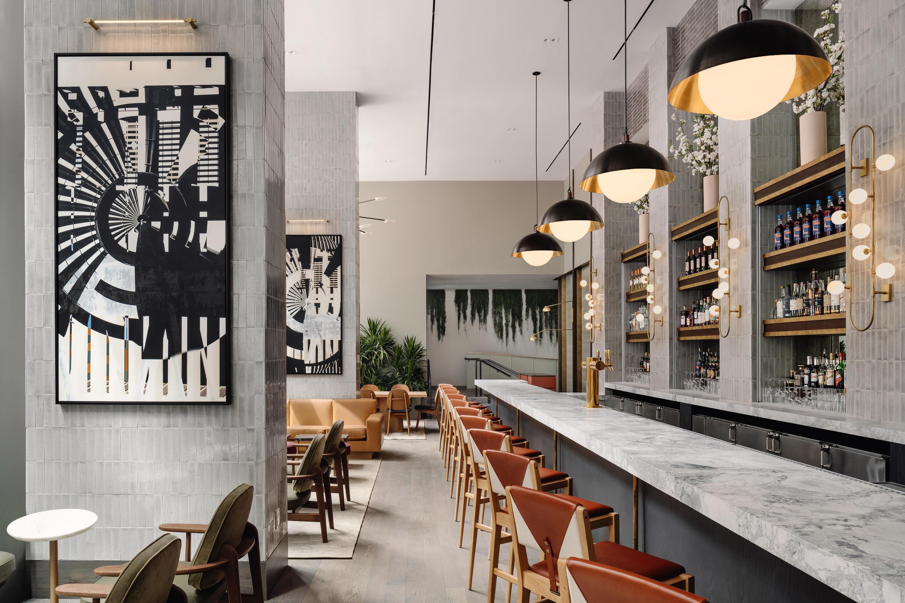 Un espace bar moderne doté d’un long comptoir, de nombreux sièges et d’œuvres d’art décoratives murales.