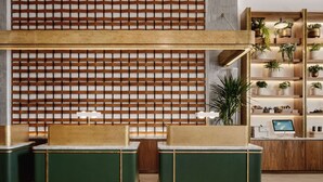 A reception area with a wooden lattice wall, green reception desks, a wooden shelving unit with plants, and a desk with a computer monitor.