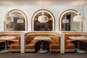 Un restaurante con tres ventanas arqueadas, cada una con una lámpara colgante. Hay tres zonas de estar con mesas y sillas.