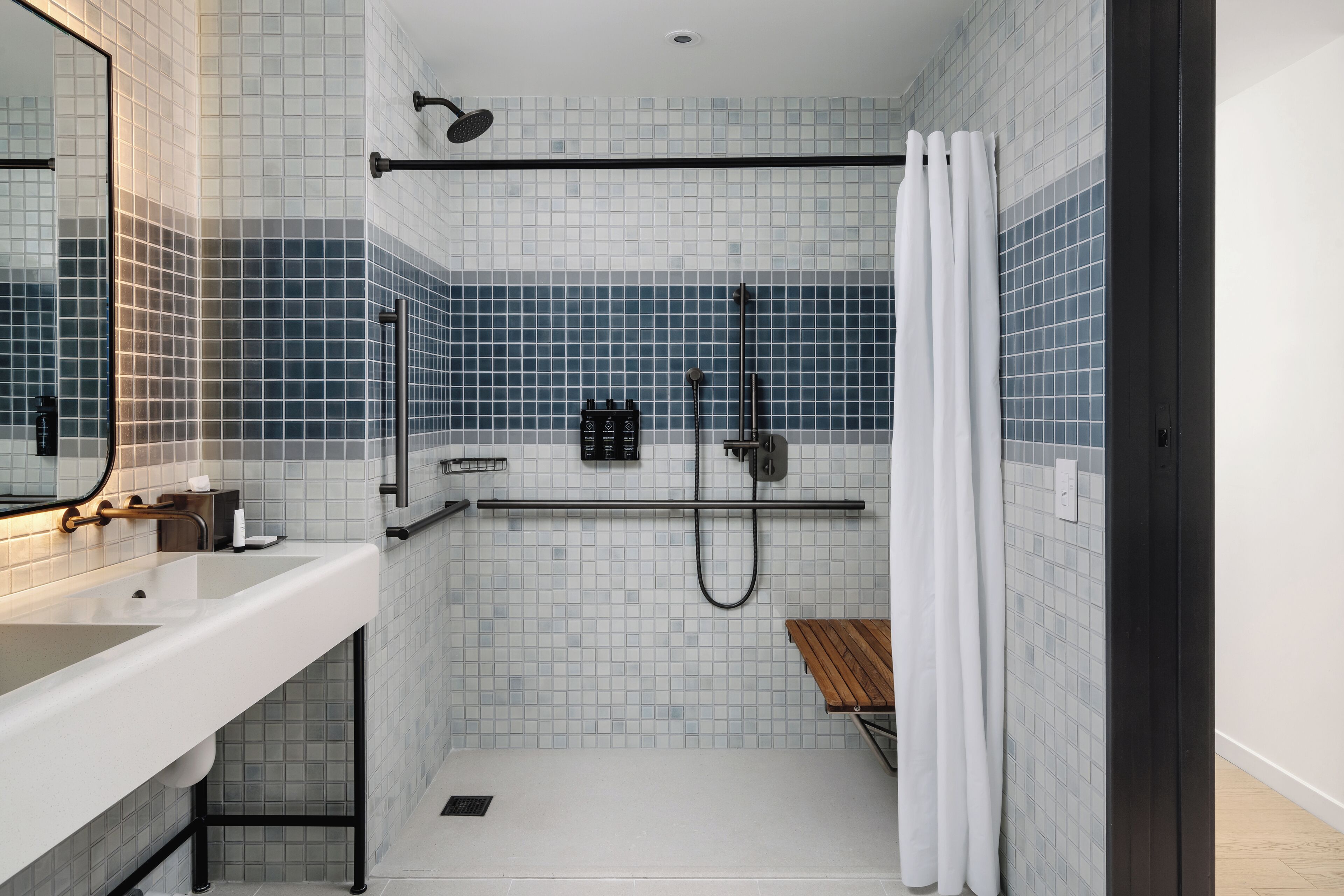 A modern bathroom with a white sink, a glass shower enclosure, and a wooden bench.