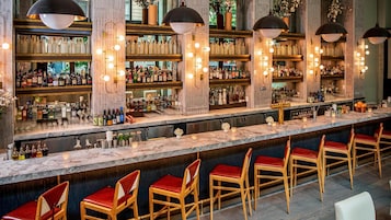 A bar area with marble countertops, multiple shelves of liquor bottles, and red upholstered bar stools.