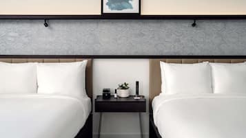 A hotel room with two beds, a bedside table with a plant, a remote control, and a small speaker.