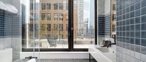 Un baño moderno con un ventanal grande, un lavabo blanco y una cabina de ducha con mampara de cristal.