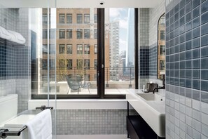 A modern bathroom with a large window, a white sink, and a glass shower enclosure.