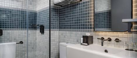A modern bathroom with a glass shower enclosure, a white toilet, a white sink with a mirror, and a towel rack with folded towels.