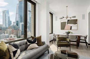 A modern living room with a sofa, dining table, and chairs, a large window with a city view, and a chandelier.