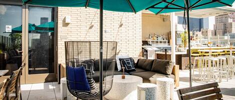 Una terraza en la azotea con mobiliario exterior, zona de bar y vistas del horizonte urbano.