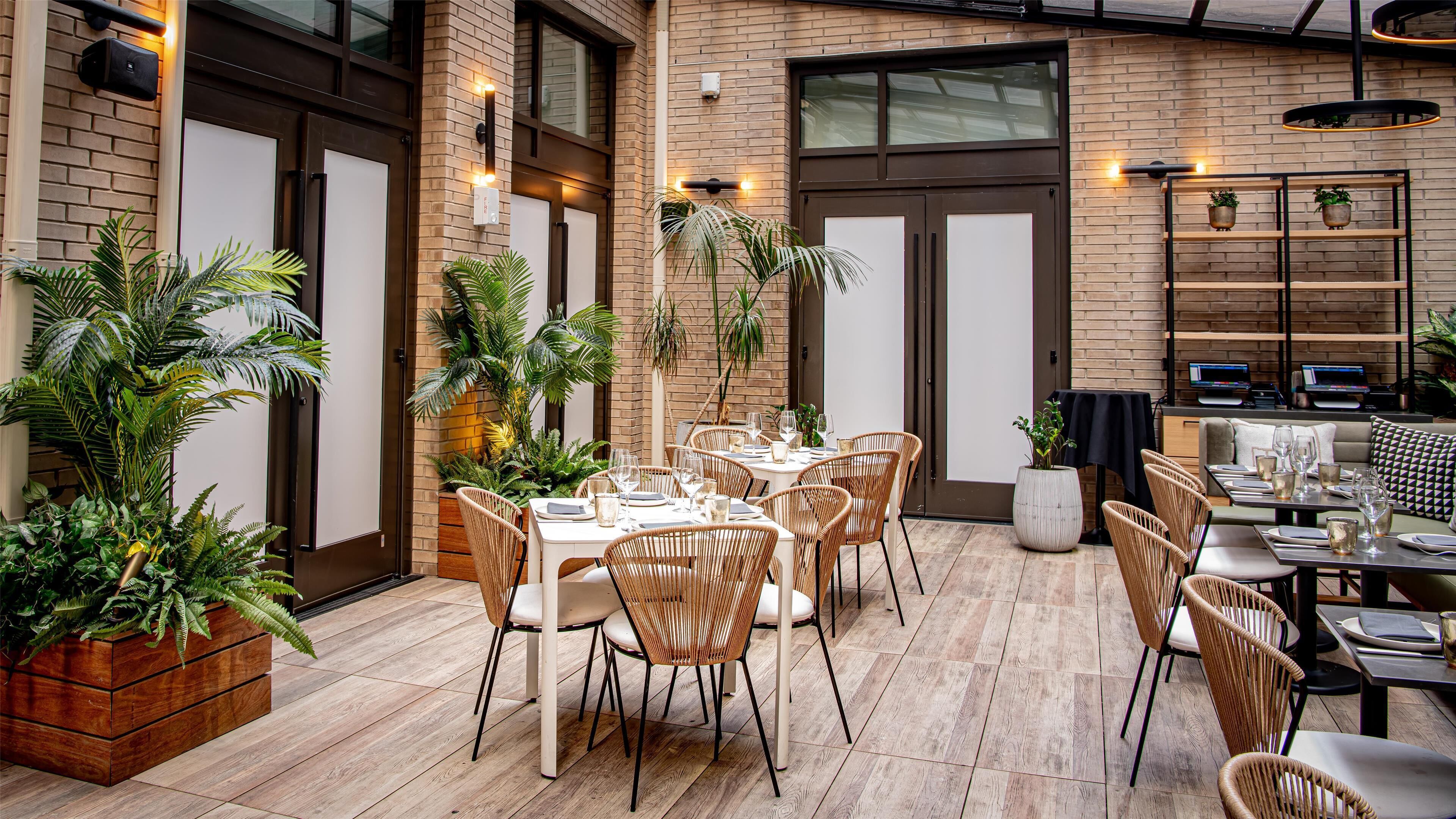 Un'area pranzo all'aperto con pareti in mattoni, pavimento in legno e sedie in vimini.