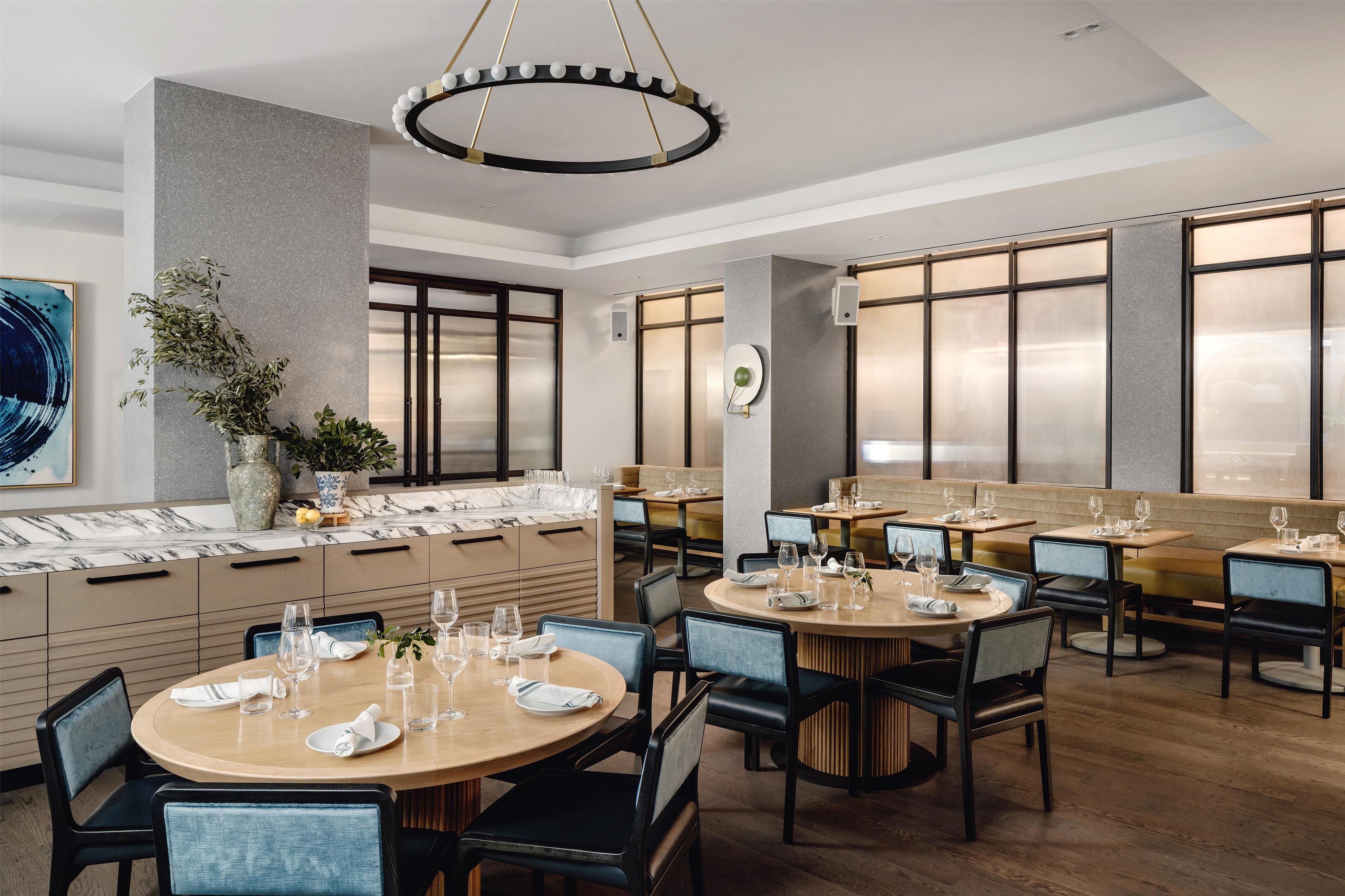 Interior de restaurante con mesas redondas, sillas y una lámpara moderna.