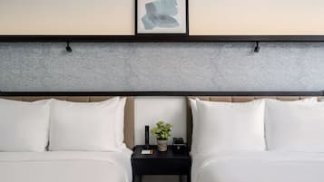 A hotel room with a bed, two pillows, a bedside table with a plant, a remote control, and a framed artwork on the wall.