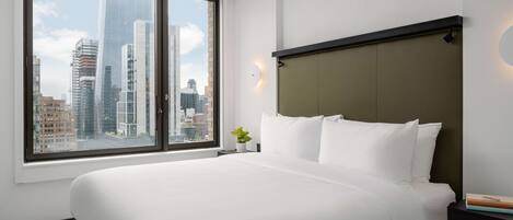 A hotel room with a large bed, a nightstand, a potted plant, and a view of a cityscape through a large window.