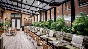 A restaurant with a long dining table, cushioned seating, and a glass ceiling. - Arlo Midtown (New York)