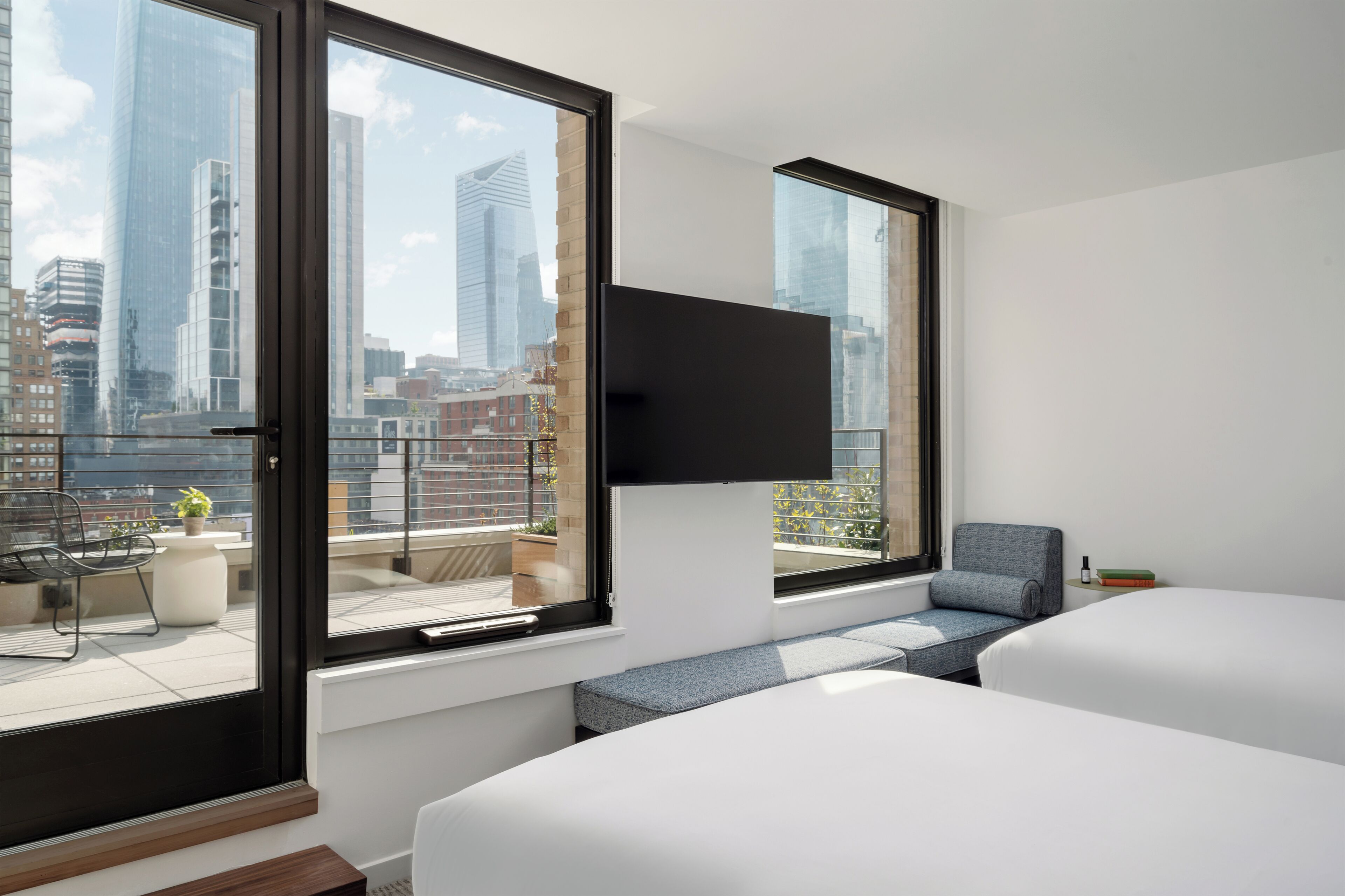A modern hotel room with large windows, a flat-screen TV, a sofa, and a bed.