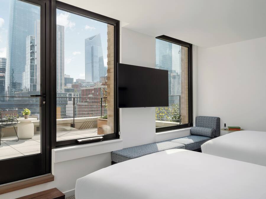 A modern hotel room with large windows, a flat-screen TV, a sofa, and a bed.