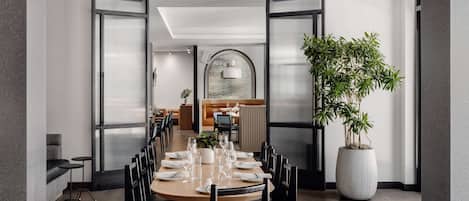 A modern dining area with a long table set for six, black chairs, and a large potted plant.