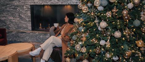 A person seated by a fireplace with a Christmas tree in the foreground.