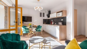 A modern living room with a sofa, a dining table with chairs, and a kitchen area with a microwave and cabinets. - Apartamenty Bory 6a (Zakopane)
