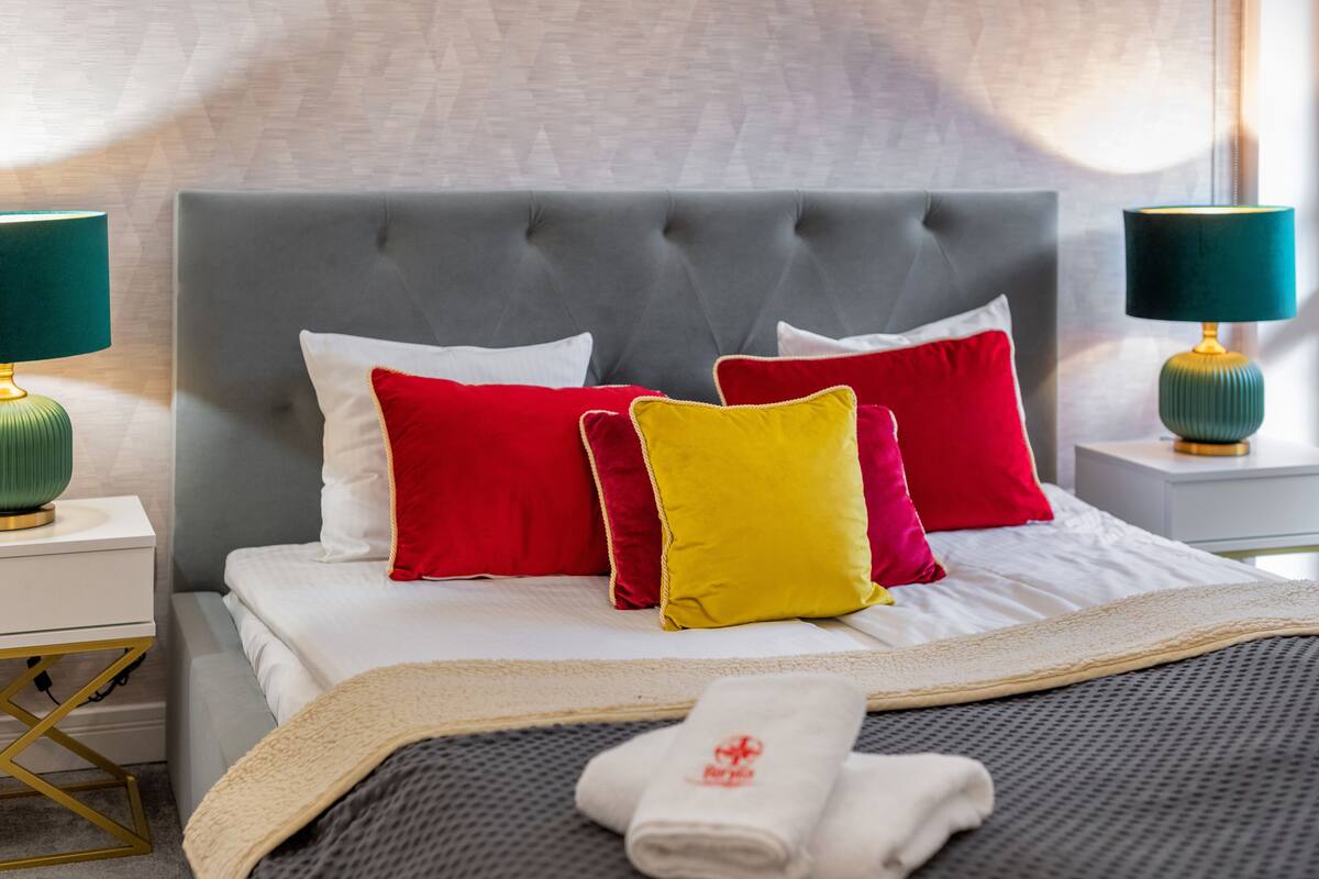 A neatly made bed with a grey upholstered headboard, white bedding, and multiple colorful pillows.