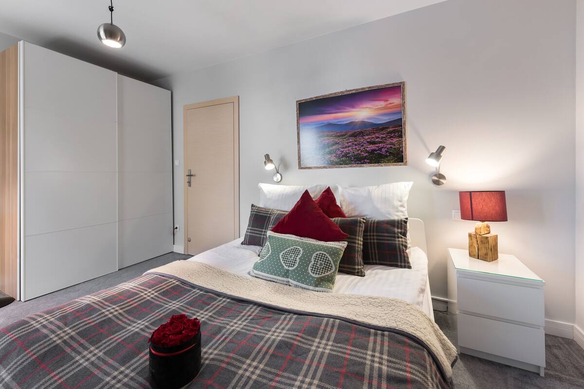 A bedroom with a bed, a nightstand, a wall-mounted lamp, a painting, and a wardrobe.