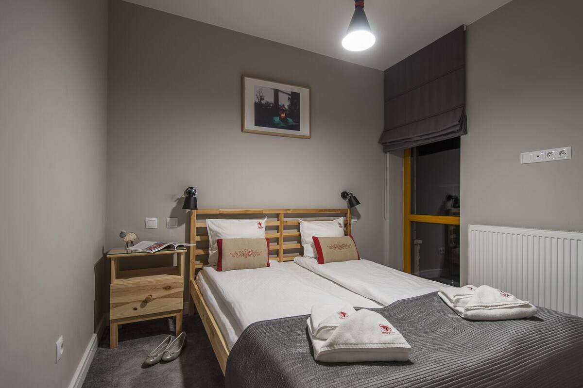 A bedroom with a bed, bedside tables, a lamp, a window with a view, and a radiator.