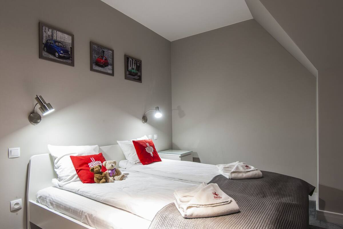 A hotel bedroom with a bed, pillows, a teddy bear, and a towel.
