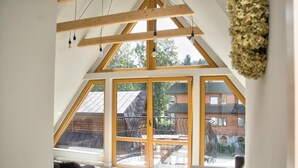 A spacious room with large windows, wooden beams, and a view of a wooden deck outside. - Apartamenty Bory 6a (Zakopane)