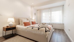 A bedroom with a bed, bedside table, lamp, and a window with curtains. - Savory Black Apartment, Sete Rios, Lisbon!New! (Lisboa)