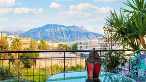 A balcony with a glass table, a red lantern, and a view of mountains and buildings.