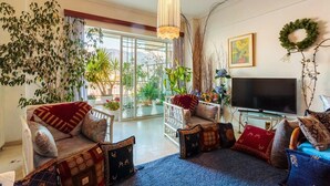 A living room with two sofas, a TV, and a large window with plants.