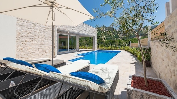 A poolside area with lounge chairs and an umbrella, a stone wall, and a view of greenery. - Villa Hvar Beauty with Swimming Pool (Jelsa)