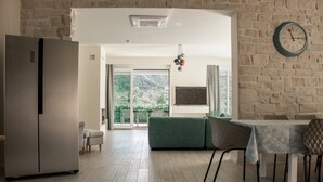 A modern kitchen with a built-in refrigerator, a dining area with a table and chairs, and a large window offering a view of greenery and a distant building. - Villa Hvar Beauty with Swimming Pool (Jelsa)