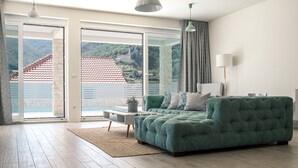 Una sala de estar moderna con un sofá verde, una mesita y vistas a un paisaje montañoso a través de amplios ventanales.