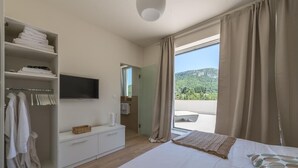 Un dormitorio con cama, armario, televisión y balcón con cortinas.