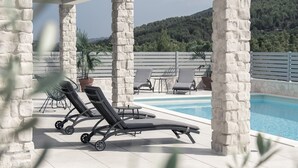 Un área junto a la piscina con sillas de descanso, una mesa y plantas en macetas.