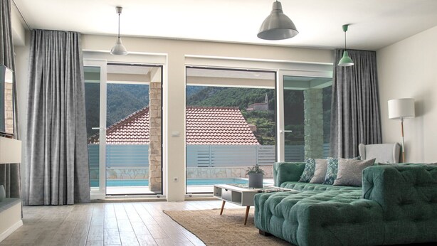 Amplia sala de estar con un sofá verde, una mesa de centro y vistas a un tejado de tejas por una puerta corrediza de vidrio.