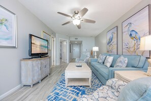 A living room with a television, a ceiling fan, a sofa, a coffee table, and artwork on the walls.