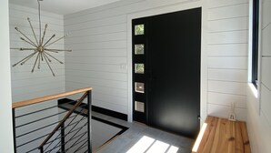 A modern interior with a staircase, a black door, and a ceiling light fixture.