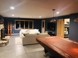 A living room with a sofa, a pool table, a stone fireplace, and skis leaning against the wall. - Best View on Malletts Bay (Colchester)