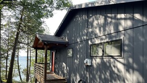 A cabin with a wooden deck, a covered porch, and a view of the lake.