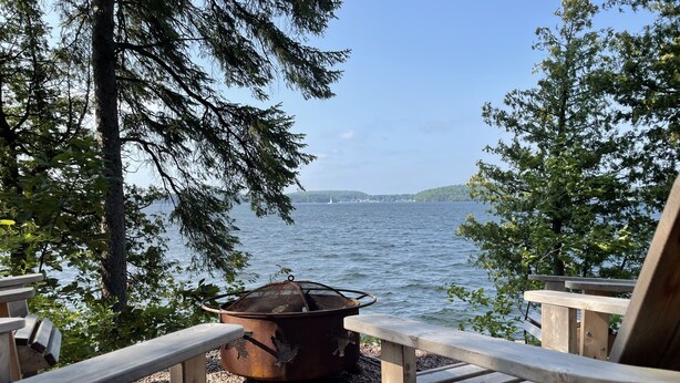A lakeside view with wooden chairs and a fire pit.