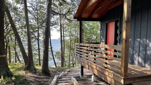 A wooden deck leading to a cabin with a red door, surrounded by trees and a view of the water.