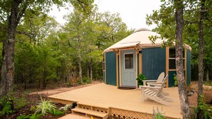 A wooden deck with a door and a chair, surrounded by trees. - Relax in your own secluded Yurt Cabin nestled into a 200+ acre Property! (Bastrop)