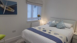 A bedroom with a bed, a window with blinds, a radiator, a nightstand, and a green chair. - Blue Horizons with uninterrupted Panoramic sea views 2 mins walk from beach (Weymouth)