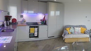 A modern kitchen with a built-in oven and a dining area with a glass table. - Blue Horizons with uninterrupted Panoramic sea views 2 mins walk from beach (Weymouth)