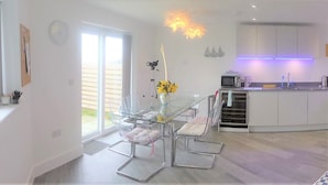 A modern kitchen with a glass dining table and chairs, a kitchen island, and a large window. - Blue Horizons with uninterrupted Panoramic sea views 2 mins walk from beach (Weymouth)