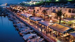 Un port de plaisance où les bateaux sont amarrés le long du quai, reliés par une passerelle couverte qui offre également des espaces de repos en plein air.